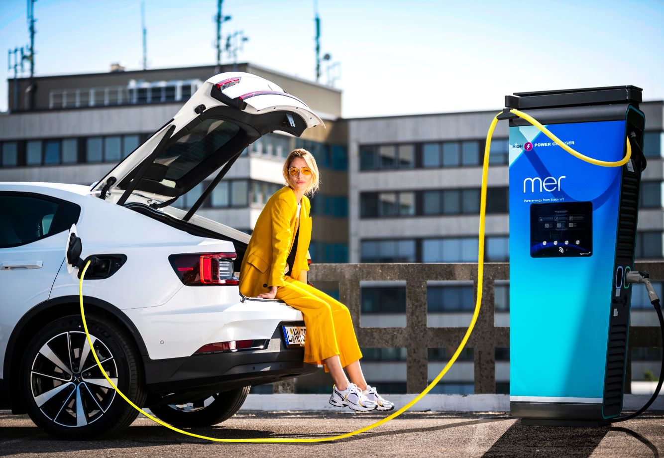 Woman sitting on boot of EV while charging car - Commercial EV Infrastructure