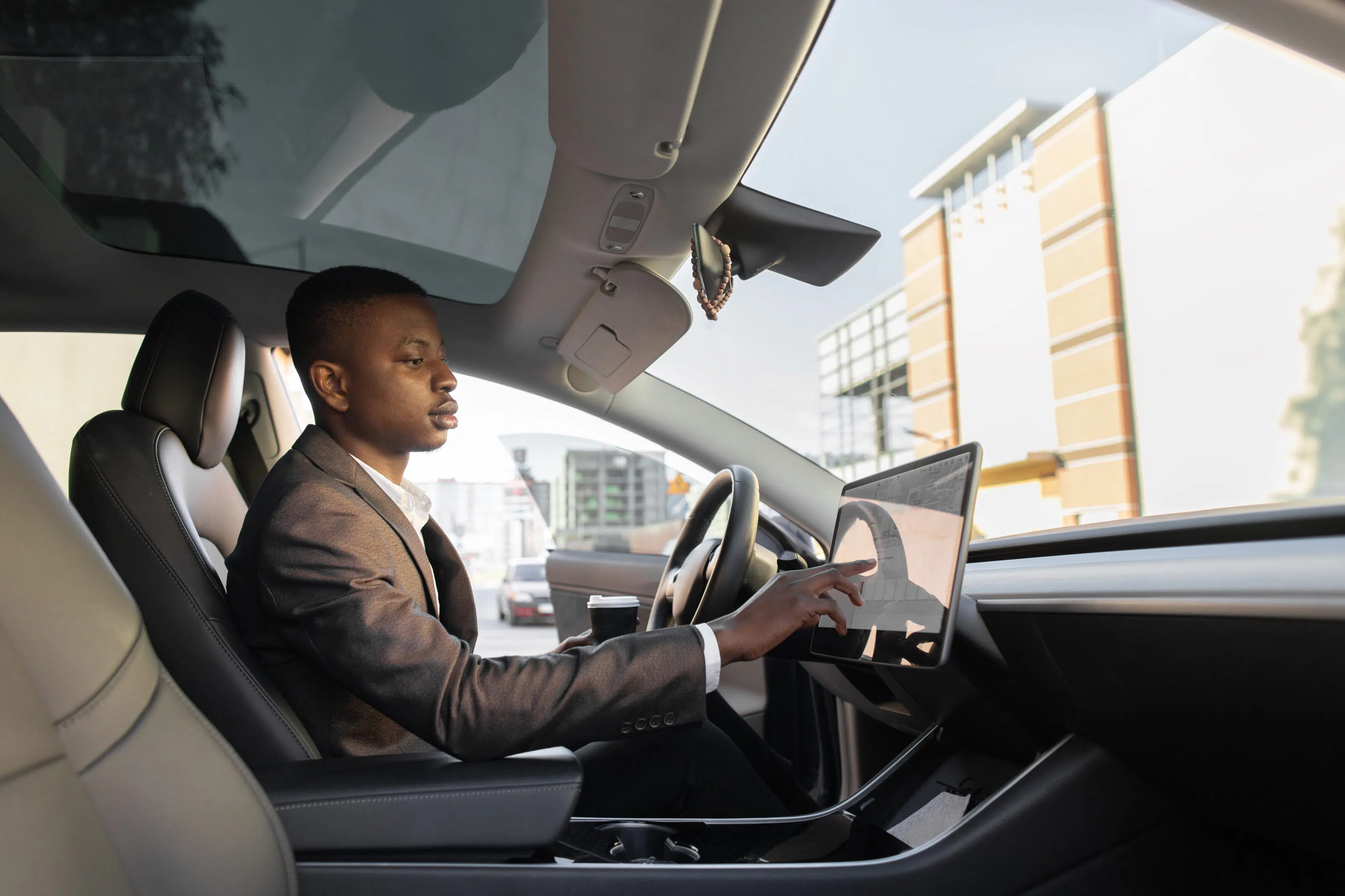 Businessman touches the touchscreen in his new high-tech electric vehicle while drinking takeaway coffee.