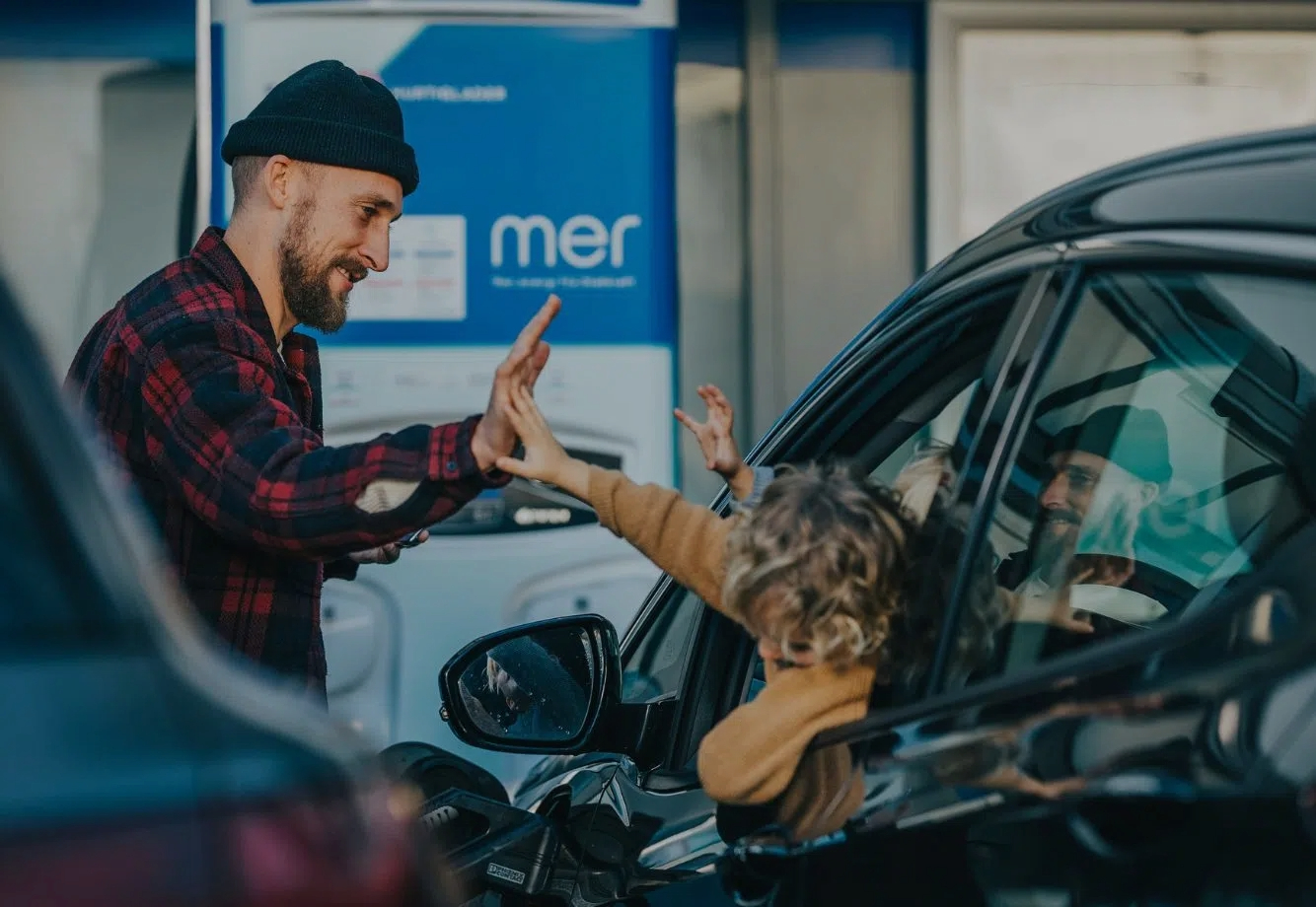 Man standing by Mer EV charger, high-fiving young children in car