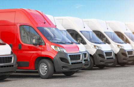 A row of white delivery vans with a red van in the middle.